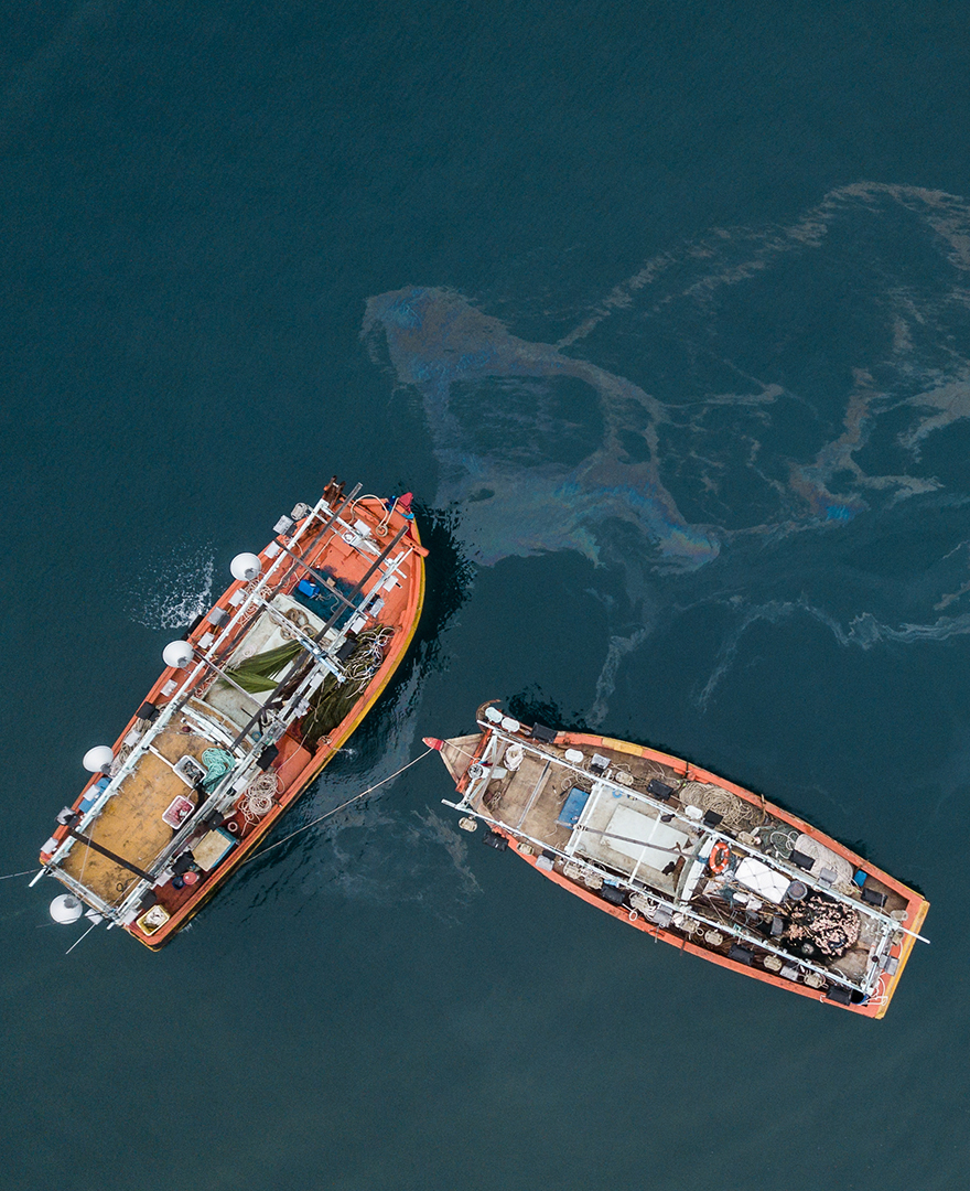 Oceanic pollution is depicted as two fishing boats release fuel into the water.